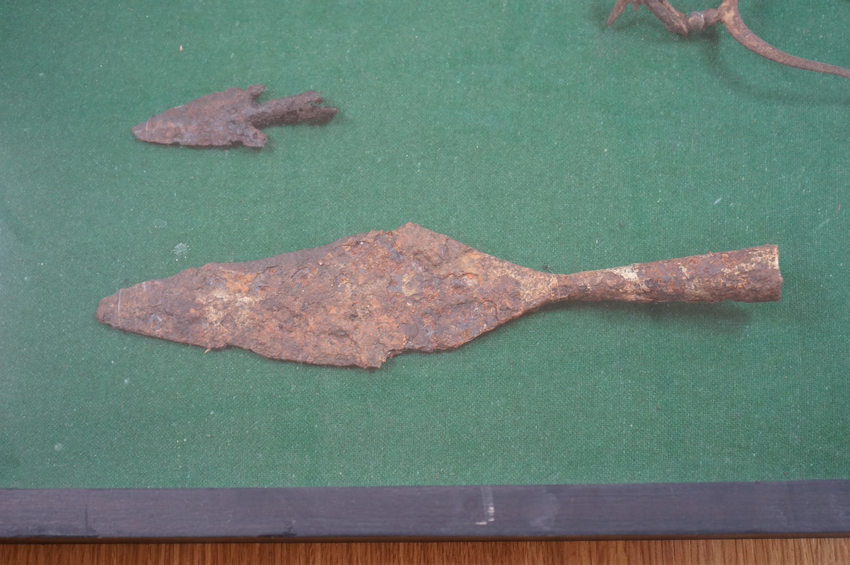 A display cabinet with a collection of antiquities comprising; medieval spur, spear and arrow heads, 53cm high. Condition - fair, relic condition